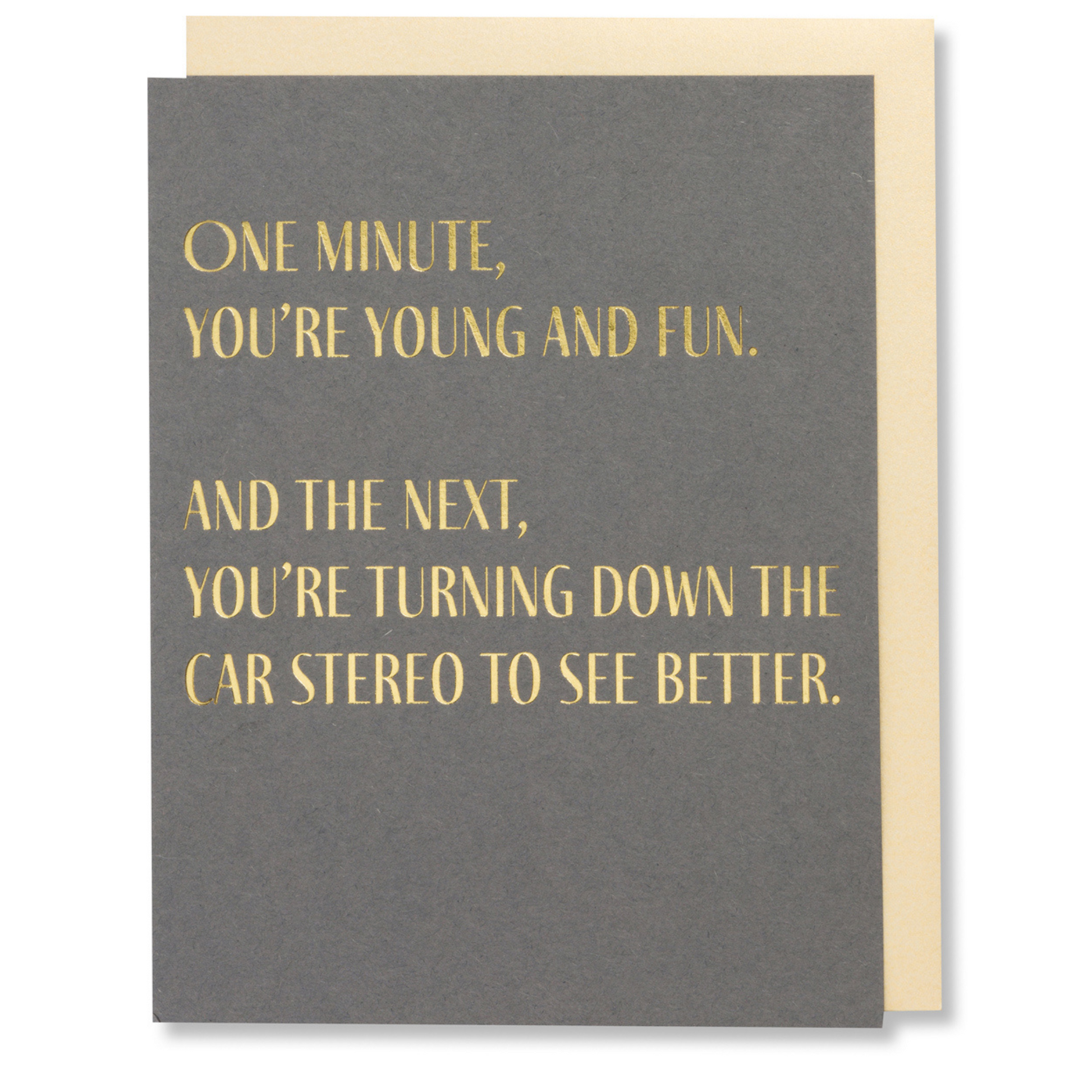 Gray birthday card with gold foil text that reads, “One minute you're young and fun. And the next, you're turning down the car stereo to see better,” paired with a white envelope.