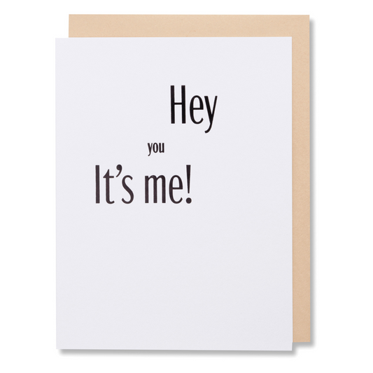 Greeting card with bold black foil text 'Hey You, It’s Me' on white paper, versatile for any occasion, shown with tan envelope